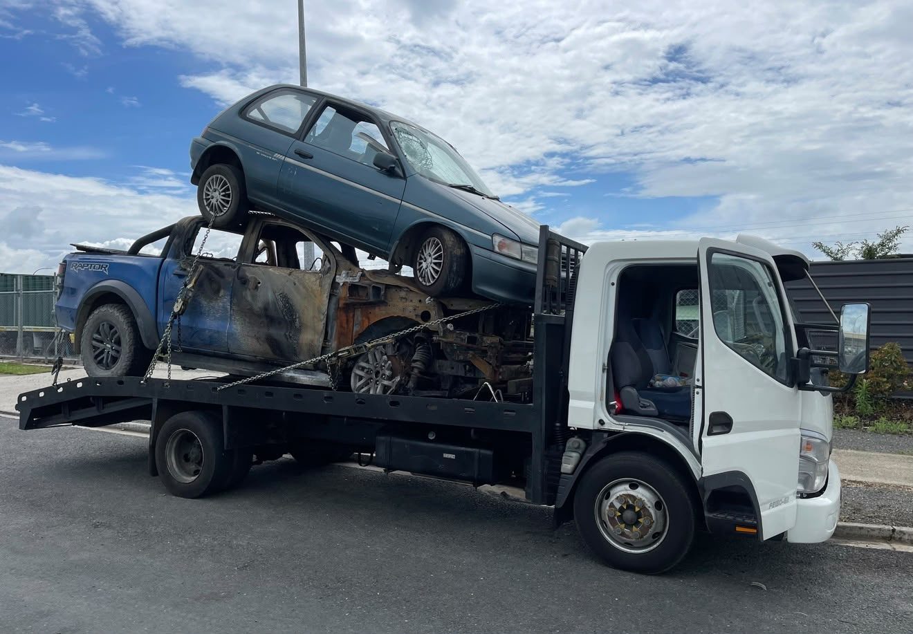Burnt-out ute and a scrap hatchback loaded on a flatbed truck for cash-for-scrap-cars removal in Queenstown
